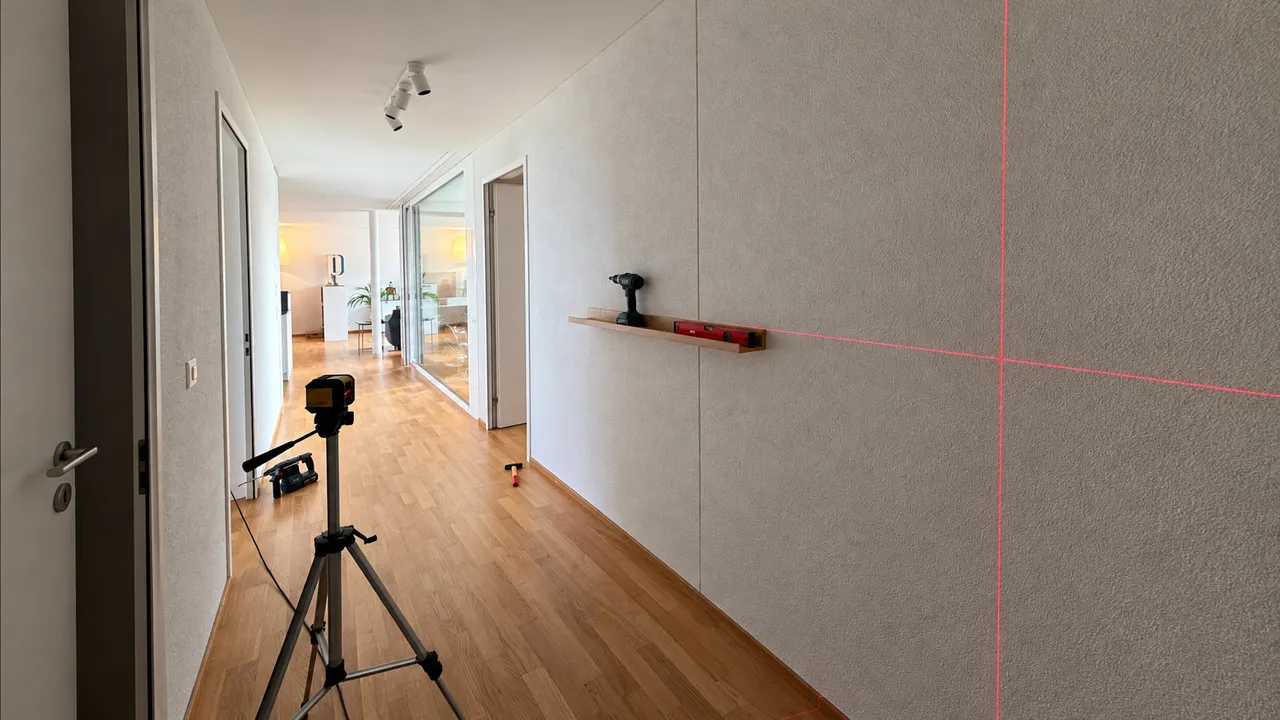 Kreuzlinienlaser auf einem Stativ im Flur einer Wohnung, rote Laserlinien an der Wand für die Montage