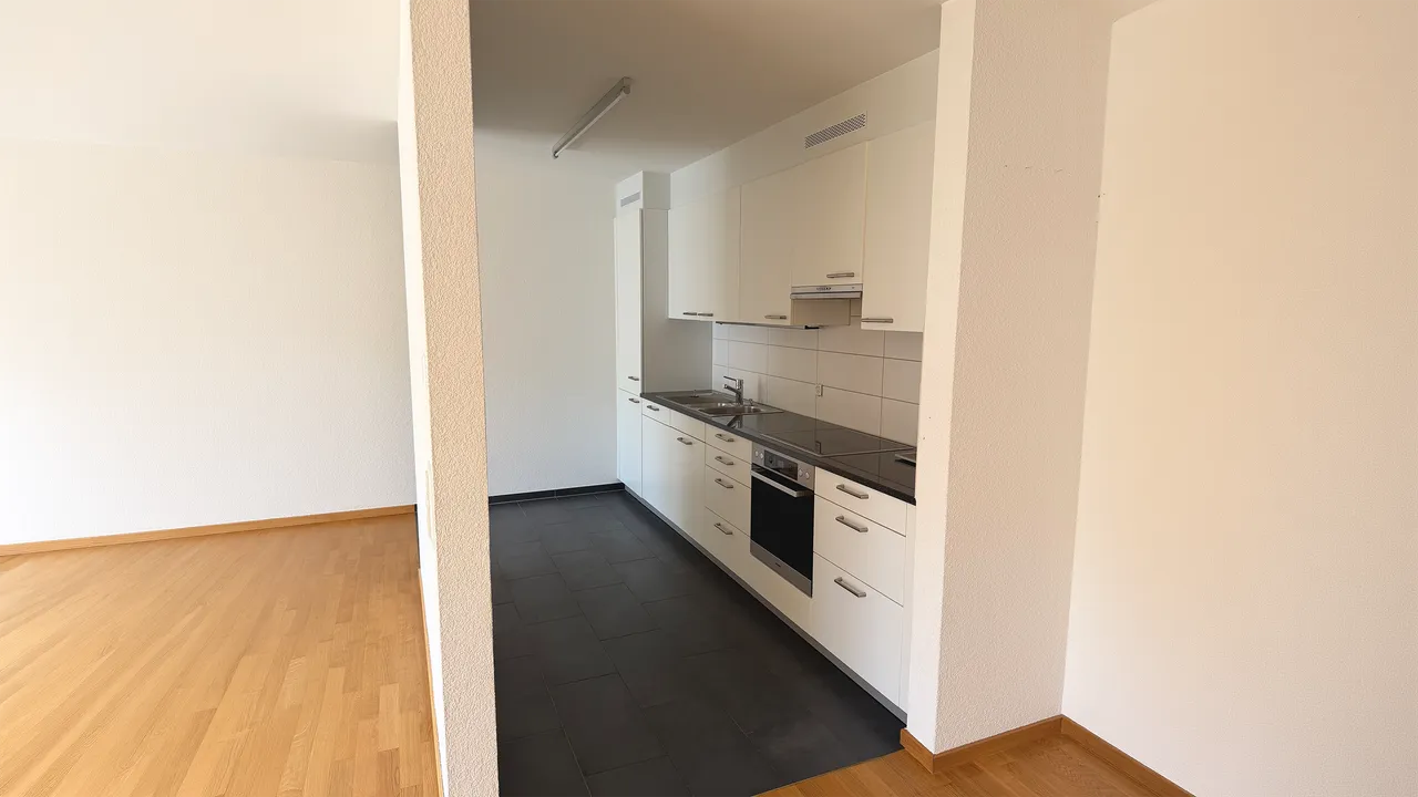 Leere Wohnung mit weisser Einbauküche und Parkettboden