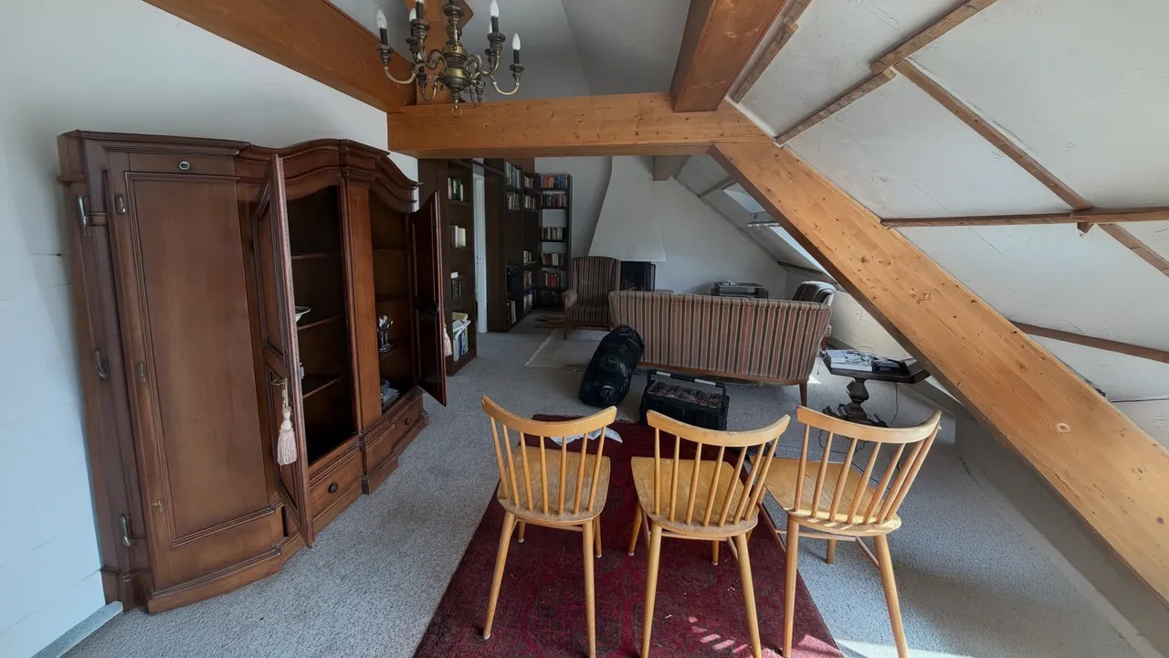Wohnzimmer im Dachgeschoss vor der Entrümpelung mit antikem Holzschrank, Stühlen, Sofa, Bücherregalen und sichtbaren Holzbalken.