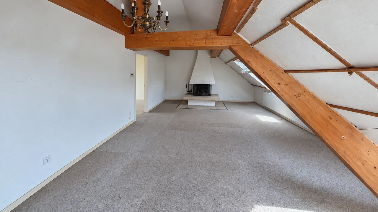 Aufgeräumtes und gereinigtes Dachgeschoss-Wohnzimmer mit freigeräumter Fläche, Kamin und sichtbaren Holzbalken.